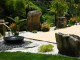 A lovely Japanese Garden featuring big rocks and a water feature next to the patio
